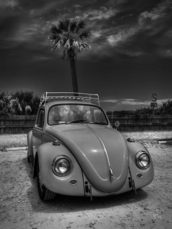 A highly customized Volkswagen Beetle, complete with roof rack, is parked at a public beach under beautiful, blue skies on Tybee Island, Georgia. 